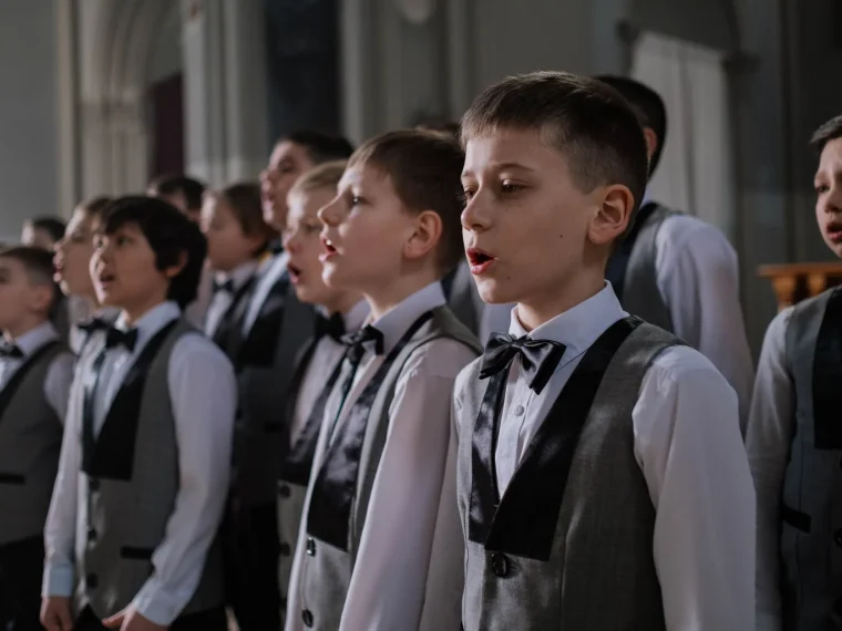 A young singer in a black choir robe performing on stage under soft light.